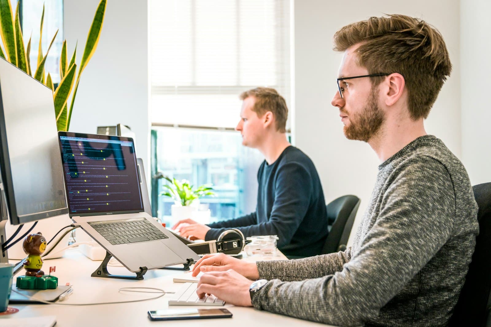 Photo: Alvaro Reyes, Unsplash Two engineers working side by side at desks with laptops and a large monitor